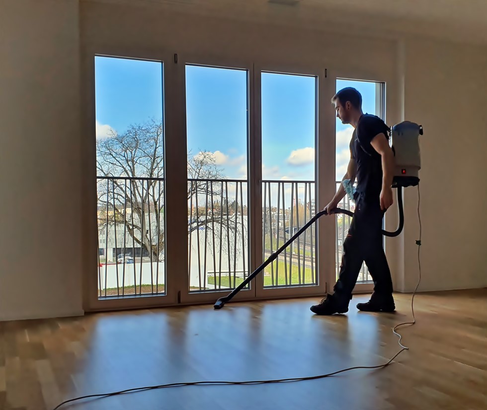 Im Rahmen der Endreinigung in Luzern bedient ein Ever-Clean-Professional sorgfältig einen Staubsauger auf dem Boden eines lichtdurchfluteten Apartments, während die glänzenden Fenster im Hintergrund den hohen Reinigungsstandard unterstreichen.